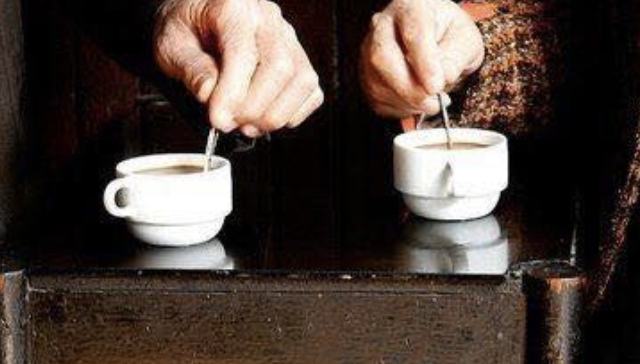 Two hands stirring cups of coffee on a wooden bench